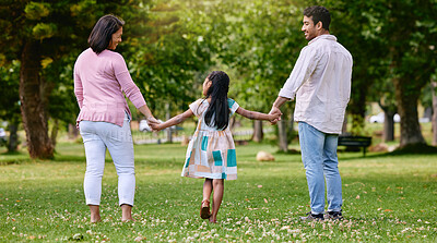Buy stock photo Rear view of parents and little girl holding hands while walking in park on a sunny day. Loving and caring family with one child bonding and having fun outdoors