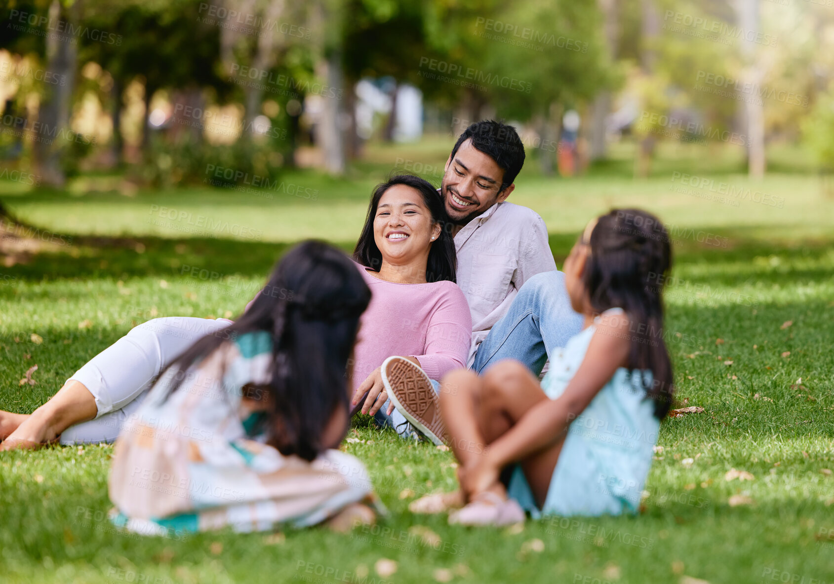 Buy stock photo Portrait of happy asian couple lying together on grass. Kids playing while watching their loving parents spending time together at the park