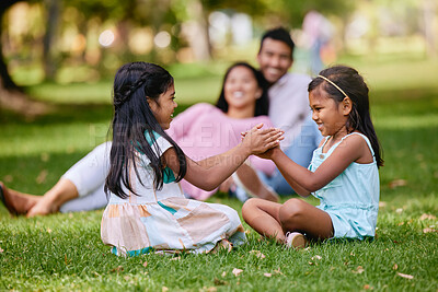 Buy stock photo Two little girls playing a clapping game while sitting in the park on a sunny day. Parent watching their daughters get along. Small sibling sister friends playing together on the grass