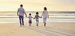 Family with two children holding hands while walking on the beach at sunset. Mixed race parents spending the day at the beach with their daughter and son while enjoying summer vacation