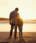 Rear view shot of father and daughter spending time together at the beach at sunset. Loving father embracing little girl while standing together by the sea