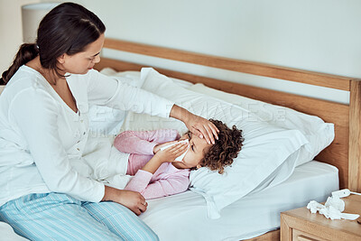 Buy stock photo Sick mixed race girl blowing runny nose with tissues in bed at home. Worried mother using hand to feel the high body temperature on her little daughter's forehead for symptoms of fever, flu or covid