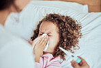 Mixed race little girl blowing her nose while laying in bed feeling unwell. Little sick daughter being looked after her mother. Mom checking temperature of female child who is ill