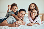 Portrait of happy mixed race family with two children lying on the bed at home. Smiling couple bonding with their son and daughter in the morning at home. Adorable boy and girl lying on their mother and father