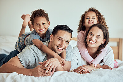 Buy stock photo Portrait of happy mixed race family with two children lying on the bed at home. Smiling couple bonding with their son and daughter in the morning at home. Adorable boy and girl lying on their mother and father