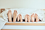Closeup of feet of family lying in bed. Bare feet of parents and children sticking out in bed. Family with two children relaxing in bed together. Kids sleeping in bed with their parents