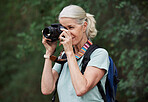 A mature caucasian woman taking pictures with her camera while out hiking. Senior female using her wireless digital camera to take photos in nature during a hike outdoors