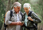 A mature couple using a cellphone while out on a hike together. Senior caucasian husband and wife using a wireless device in a forest