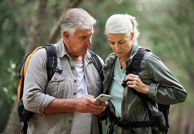 A mature couple using a cellphone while out on a hike together. Senior caucasian husband and wife using a wireless device in a forest