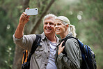 Portrait of a senior caucasian couple smiling and taking a selfie with a smartphone in a forest during a hike in the outdoors. Man and wife showing affection and holding each other during a break in nature