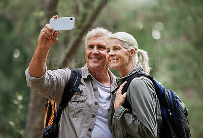 Portrait of a senior caucasian couple smiling and taking a selfie with a smartphone in a forest during a hike in the outdoors. Man and wife showing affection and holding each other during a break in nature