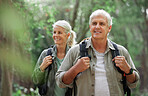 A mature caucasian couple out for a hike together. Senior man and woman smiling and walking in a forest in nature