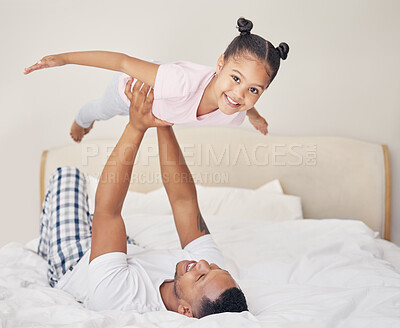 Joyful young father lying on bed, lifting excited happy little child daughter at home. Carefree family having fun in bedroom