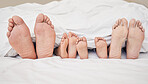 Closeup of feet of family lying in bed. Bare feet of parents and children sticking out in bed. Family with two children relaxing in bed together. Kids sleeping in bed with their parents