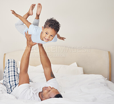 Buy stock photo Joyful young single father lying on bed, lifting excited happy little child son at home. Little boy pretending to fly while having fun in bedroom with parent
