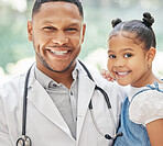 Portrait of handsome young black paediatrician holding adorable little girl in hands, cute child and doctor smiling during medical check up in clinic