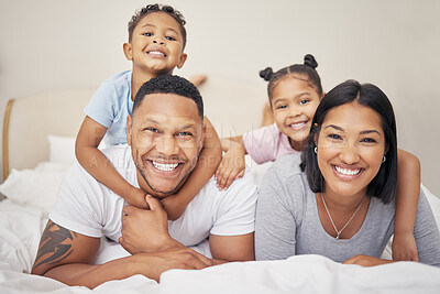 Buy stock photo Portrait of a cheerful family lying together on bed. Little boy and girl lying on their parents laughing and having fun. Mixed race couple bonding with their son and daughter. Hispanic siblings enjoying free time with their mother and father