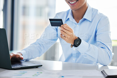 Close up of unknown businessman using a credit card to make a purchase online using his wireless laptop in a office. Cheerful male smiling while shopping online at work while sitting at a desk