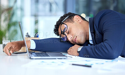 One exhausted mixed race businessman wearing glasses while sleeping at his desk in an office. Young entrepreneur feeling overworked, tired and demotivated. Lazy man slacking and ignoring deadlines by taking a nap. Burnout and stress in the workplace
