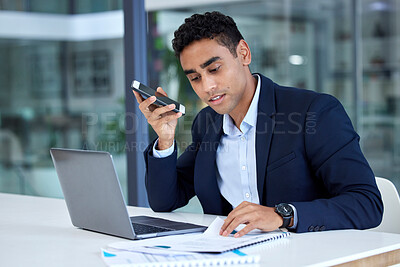 One mixed race businessman talking on cellphone with audio loudspeaker while reading document notes and browsing on laptop in an office. Hispanic entrepreneur recording voice note memos on phone while planning deadlines with paperwork reports