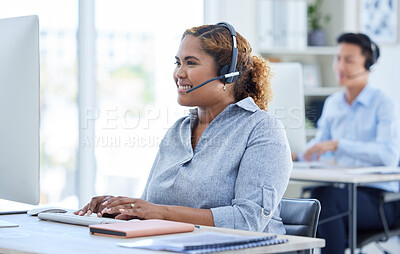 One happy young mixed race female call centre telemarketing agent talking on a headset while working on a computer in an office. Confident and friendly african american businesswoman consultant operating a helpdesk for customer service and sales support