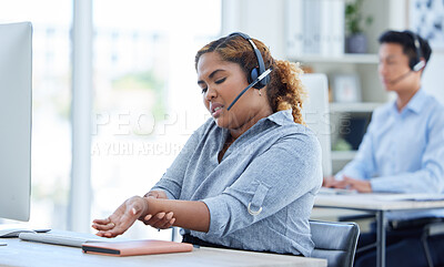 One young mixed race female call centre telemarketing agent suffering with aching wrist pain while working on a computer in an office. American american businesswoman hurt with carpal tunnel syndrome disability. Feeling discomfort cramp in arm and hand