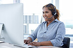 One happy young mixed race female call centre telemarketing agent talking on a headset while working on a computer in an office. Confident and friendly african american businesswoman consultant operating a helpdesk for customer service and sales support