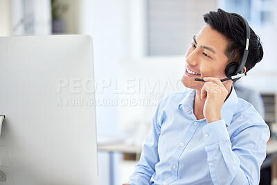 One young asian call centre agent talking on headset while working on computer in an office. Confident and happy businessman consulting and operating a helpdesk for customer sales and service support
