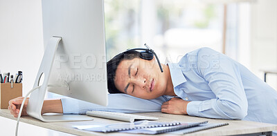 Close up of young asian businessman feeling tired and sleeping on the desk of a call center in a office. Male wearing wireless headset suffering from burnout