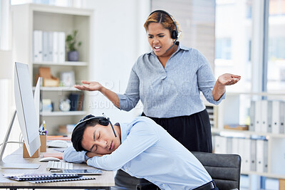 Close up of young asian businessman feeling tired and sleeping on the desk of a call center in a office while his hispanic female colleague looks confused and upset. Male wearing wireless headset suffering from burnout