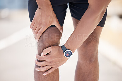 Close up of a mixed race man using his hands to hold his knee while suffering from a sports injury while running on a road. Male athlete having discomfort in his joints after a run. Wearing digital watch