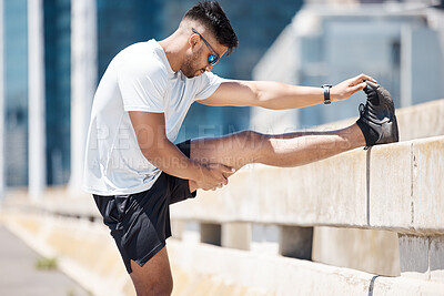 Young fitness man stretching his legs on a bridge before a run in the city. Mixed race male athlete sitting on road to stretch while touching his toes