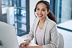 Young happy mixed race female call center agent using a desktop computer while wearing a headset answering calls and typing an email on a keyboard. One hispanic customer service worker smiling using a headset and sitting at an office desk
