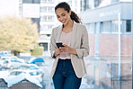 Portrait of a happy mixed race businesswoman using her phone in standing at a window in an office. One confident hispanic businessperson smiling typing a message on her cellphone at work