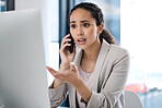 Young mixed race businesswoman on a call using her phone and desktop computer making a hand gesture looking worried in an office at work. One unhappy hispanic businesswoman sitting at a desk and talking on her cellphone at work
