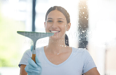 Portrait of a happy mixed race domestic worker using a squeegee on a window. One Hispanic woman enjoying doing chores in her apartment