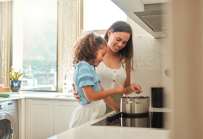 Buy stock photo Mother and little daughter preparing dinner together at home. Young mother standing with her daughter and helping her while stirring food on the stove. Mom teaching little girl to cook