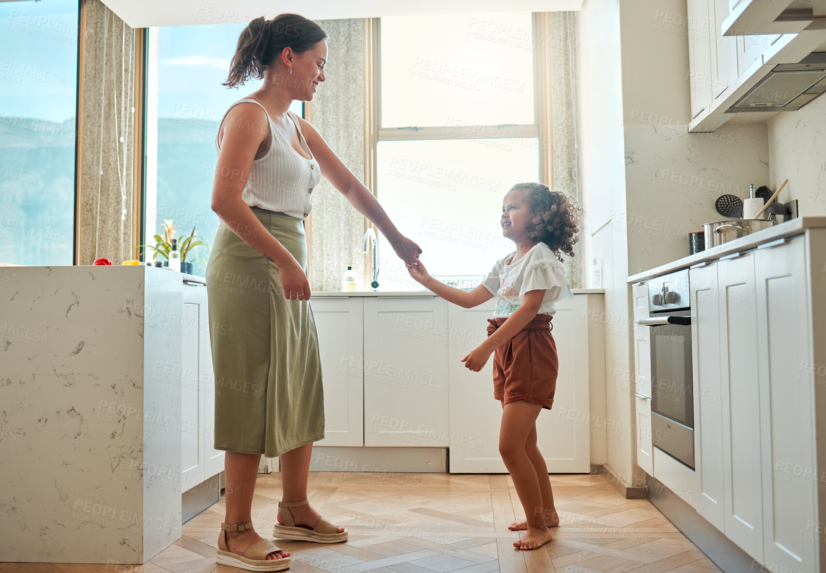 Buy stock photo Mother and little daughter dancing having active fun together in the kitchen at home. Child and nanny having fun dancing to music and playing