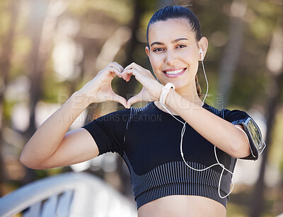 Portrait of happy young female athlete with earphones making heart shape with hands while out for a run at the park. Fit sportswoman out for a run outdoors because cardio exercise is good for the heart health