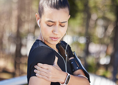 Close up view of a woman holding her arm in pain and suffering from shoulder pain during her outdoor workout. Mixed race female athlete feeling discomfort from a sports injury while exercising at the park