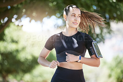 Close up of sporty young hispanic athlete wearing phone armband and smart watch while jogging at park on a sunny day. Young hispanic woman running exercising outdoors in nature