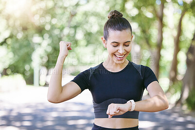 Cheerful young sporty female athlete celebrating while looking at smart watch. Hispanic sportswoman making winner gesture with clenched fist while tracking her progress while training outdoors