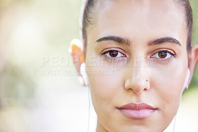 Close up face of sporty woman listening to music with earphones while standing outdoors. Portrait of beautiful hispanic woman with brown eyes and nose piercing