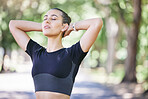 Close up of beautiful young hispanic sportswoman taking a break and stretching her neck with her hands behind her head after a workout at the park