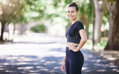 Portrait of female athlete smiling and standing with her hand on her hip while taking a break during her workout at the park. Fit young sportswoman exercising outdoors on a sunny day