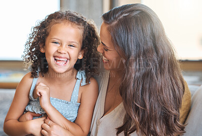 Loving mixed race mother tickling and playing with her adorable daughter as they laugh and relax on the couch at home. Sweet moment between mother and child while bonding and spending time together at home