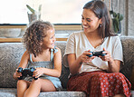 Hispanic mother and daughter playing video games together while sitting on the couch at home. Fun young mother and daughter using joysticks while playing and spending free time together on weekend