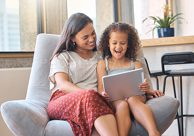 Excited little girl and loving mother sitting together on couch and using digital tablet to watch a movie or do a video call with family. Parent sitting with child while enjoying some online entertainment