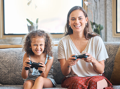 Hispanic mother and daughter battling while playing video games together while sitting on the couch at home. Fun young mother and daughter using joysticks while playing and spending free time together on weekend
