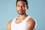 Handsome young hispanic man posing in studio isolated against a blue background. Mixed race male athlete wearing a vest and looking confident, healthy and fit. Exercising to increase his strength